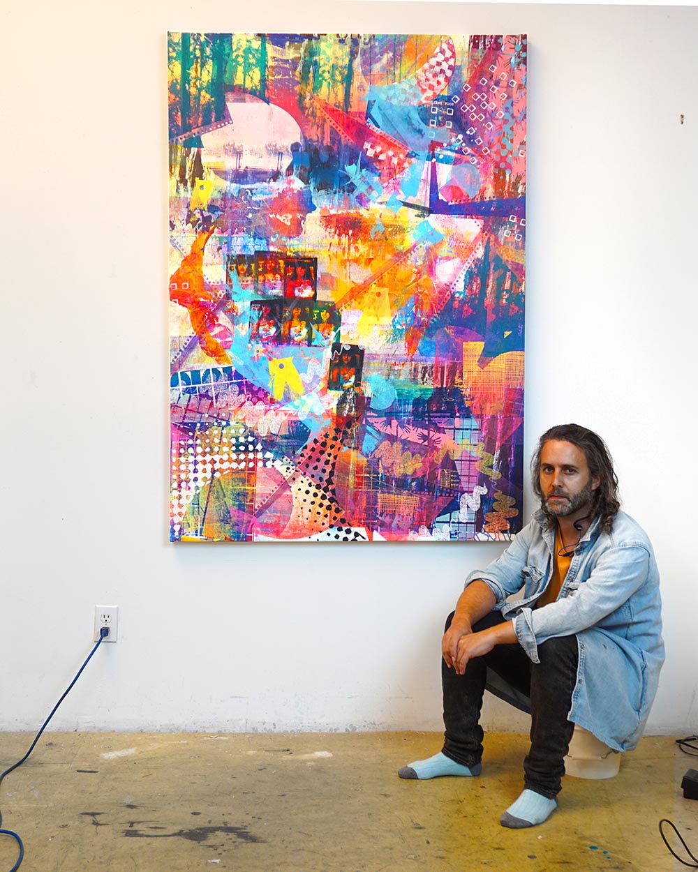 Artist Jon Fischer sitting next to his artwork